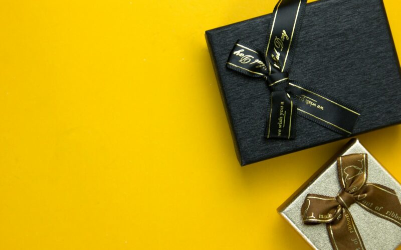 a black gift box with a gold ribbon on a yellow background